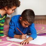 Cute school boys lying on the carpet, at home, drawing with crayons.