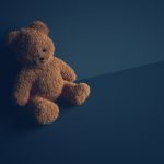 Teddy bear with torn eye sits in dark room. Child abuse and violence concept.