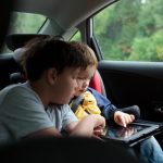 Two boys in the car using a tablet PC, younger boy sitting in the child safety seat