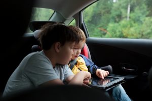 Two boys in the car using a tablet PC, younger boy sitting in the child safety seat