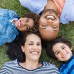 Overhead view of cheerful family lying on grass in a circle and looking at camera. High view of multiethnic family lying on grass at park. African father and hispanic mother with their smiling children