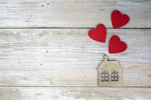 Wooden house with three red hearts on a wooden background. Love nest, love relationships. Buying a house with a young family. Affordable housing. banner. Family psychology, strong relations. copy space top view background